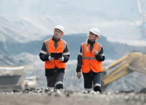 Two occupational health workers in high vis jackets and safety helmets walking outdoors and chatting at a mining site