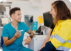 Occupational health services professional in blue shirt providing job analysis to a female worker in yellow high vis jacket