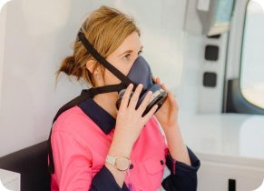Female worker with a pink shirt holding a respirator to her nose and mouth