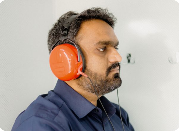 Male with beard sat with orange headphones having an occupational health hearing test
